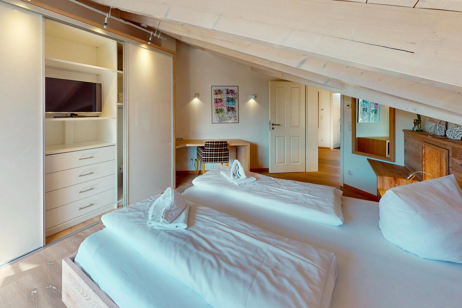 Zwei Betten mit weißen Bettwäsche, Schrank mit Fernseher und Schreibtisch mit Stuhl.