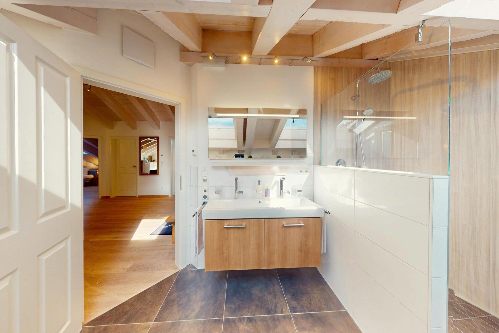 Bad mit Dusche, Waschbecken und Spiegel. Holzdecke und Fliesenboden.