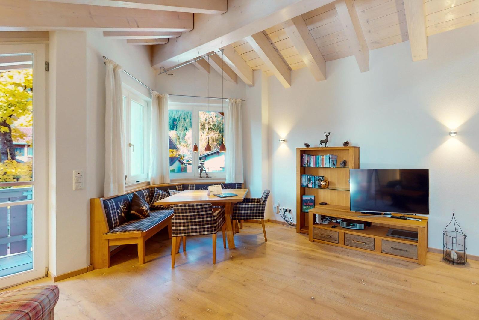 Wohn- und Essbereich mit Holzdecke, TV, Bücherregal und Fensterblick.