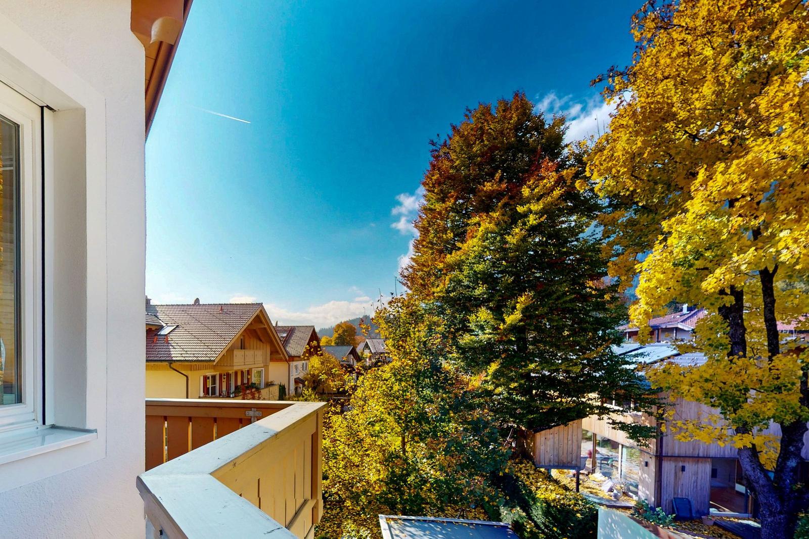 Blick vom Balkon auf einen Dorfplatz mit Bäumen im Herbst.