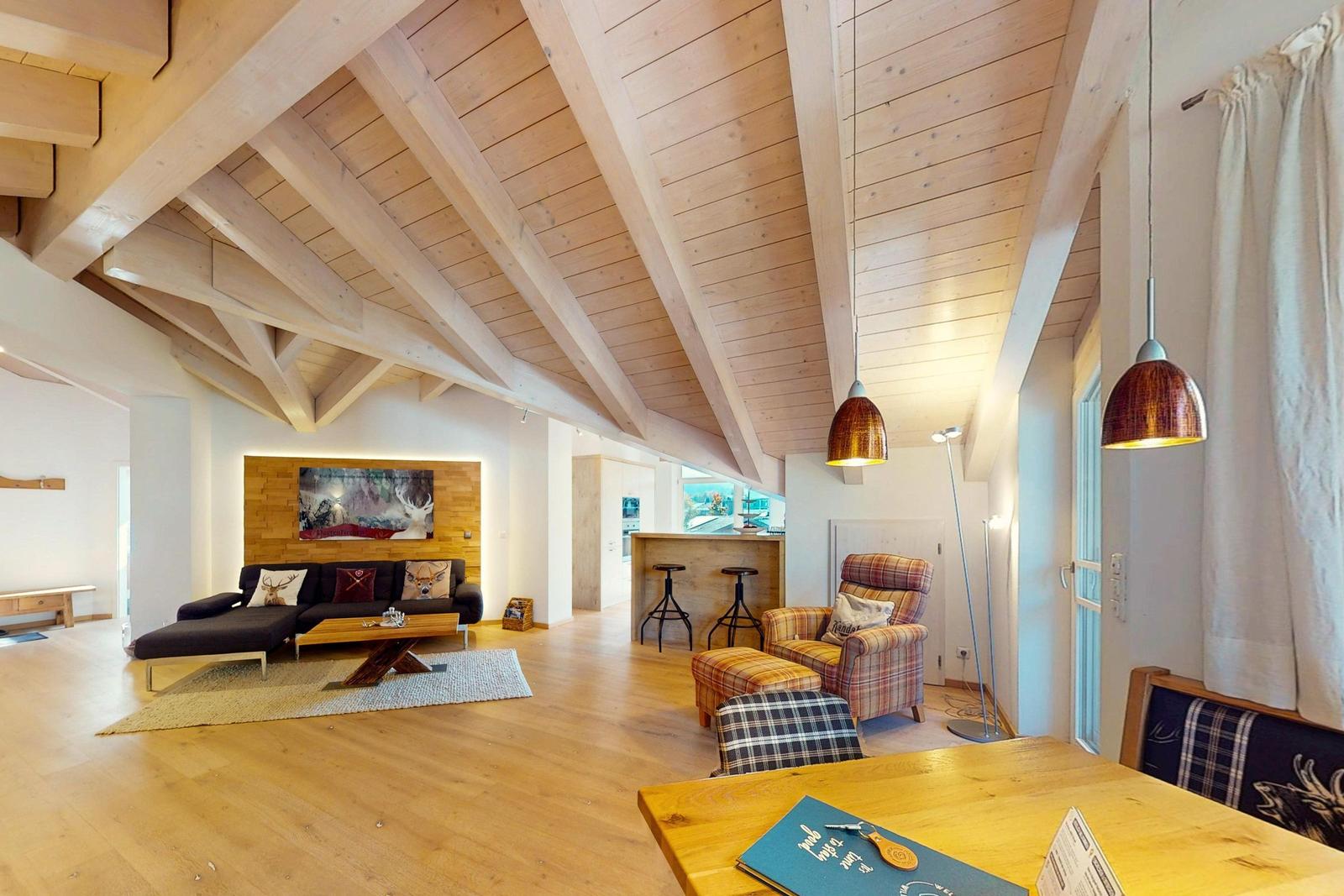 Wohn- und Essbereich mit Holzdecke, Sofa, Sessel und Esstisch.