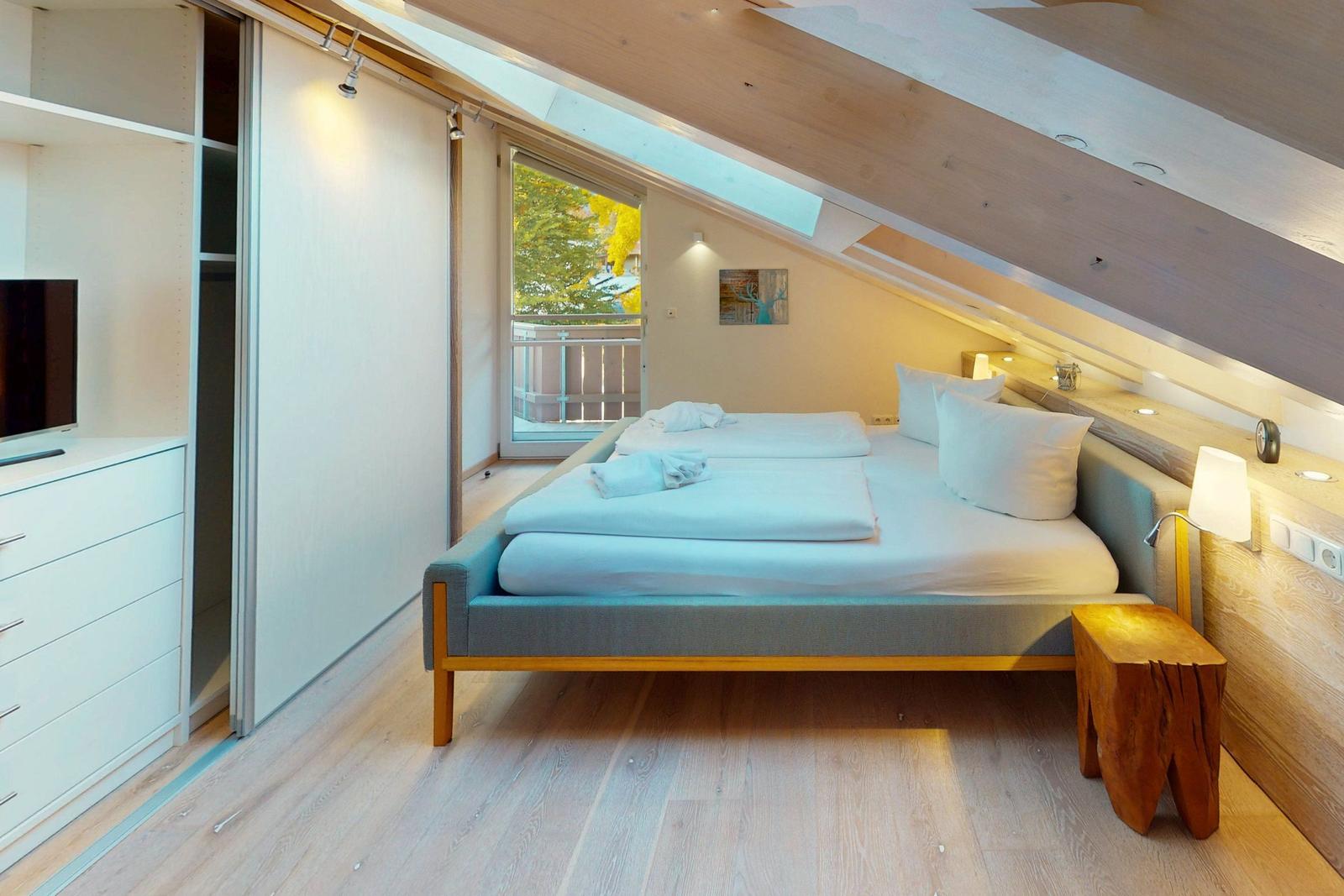 Schlafzimmer mit Doppelbett, Fenster und Holzboden. An der Wand hängt ein Bild.