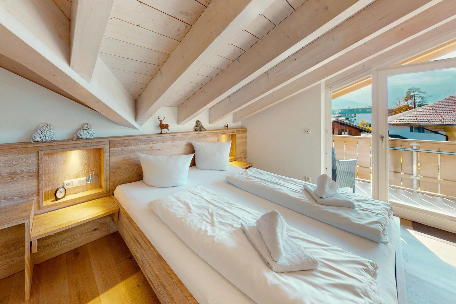 Schlafzimmer mit Doppelbett, Holzdecke und Balkonansicht.