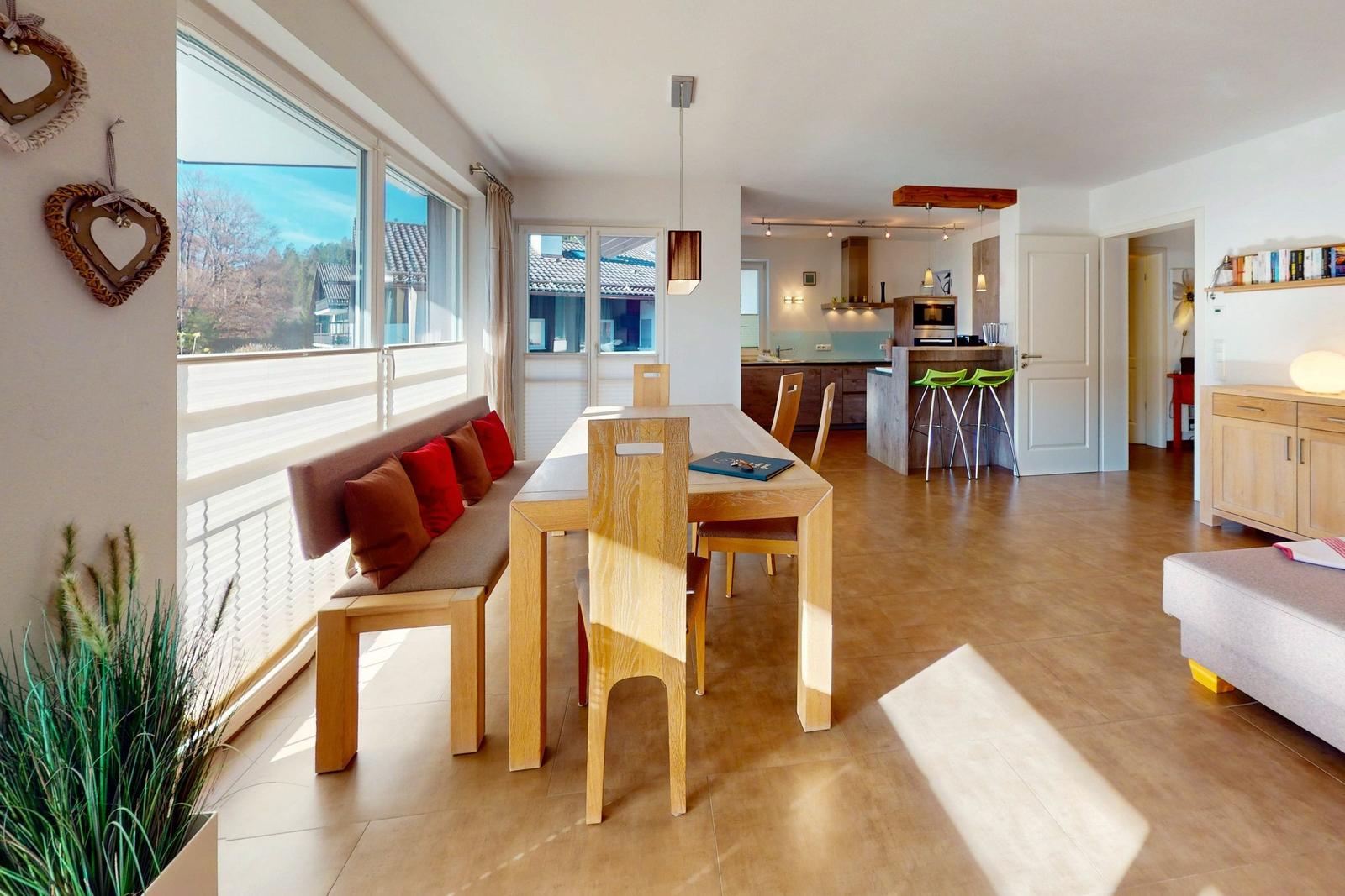 Essbereich mit Tisch, Stühlen und Fensterblick. Küche mit Kücheninsel und Barhockern.