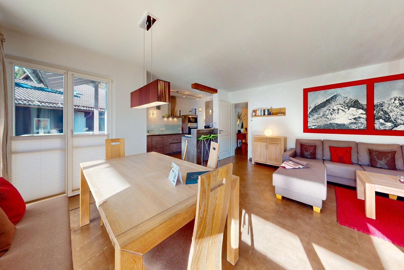 Wohn- und Essbereich mit Küchenbereich. Sofa, Tisch und Wandbild mit Bergen.