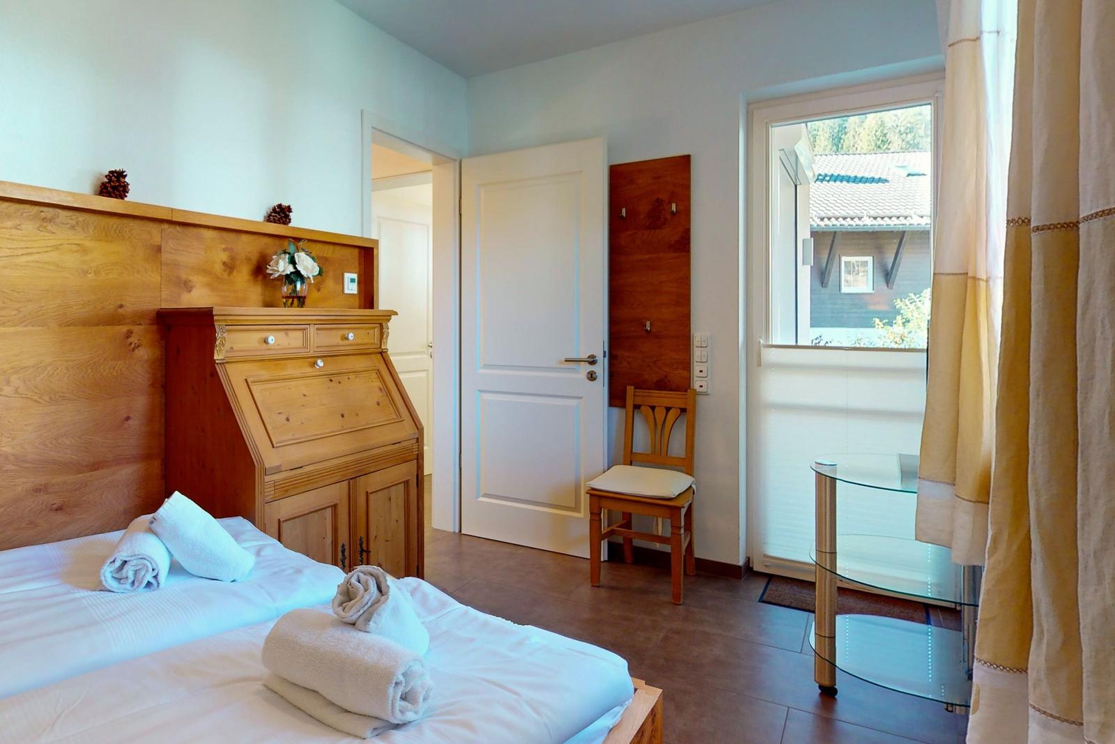 Schlafzimmer mit Holzbett, Schreibtisch und Blick auf Balkon.