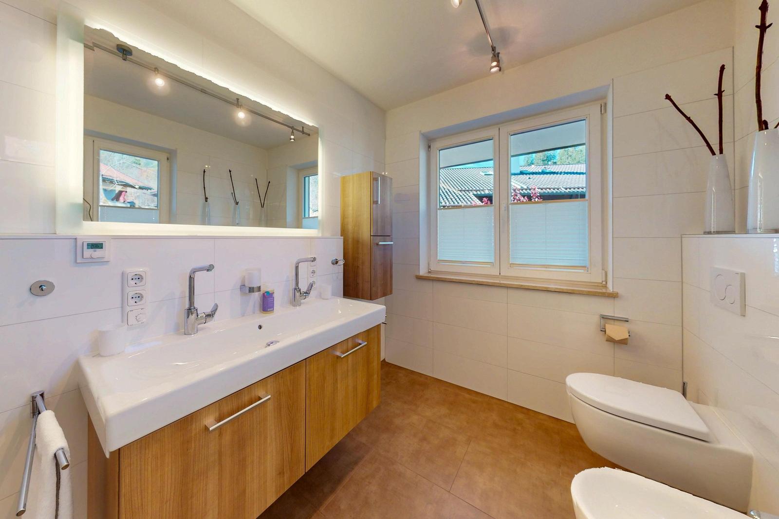 Badezimmer mit Waschtisch, Spiegel, Toilette und Fenster.