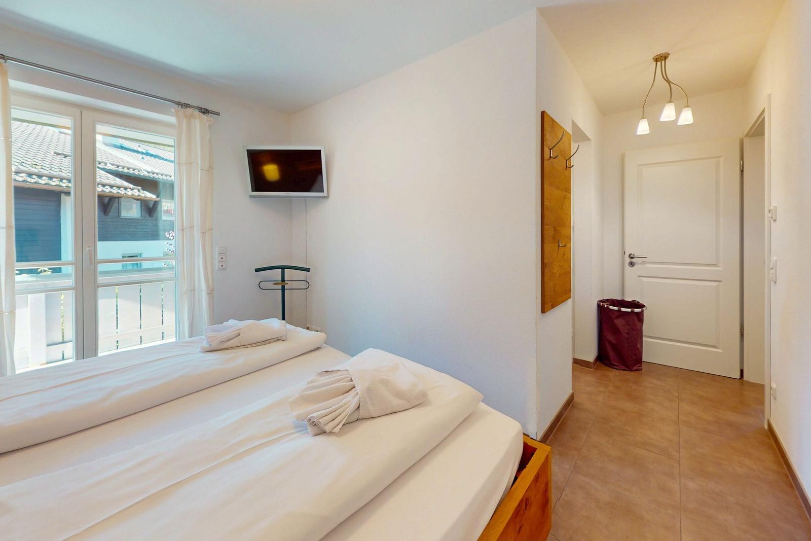 Zimmer mit zwei Betten, TV und Balkon. Helle Wände und Holzboden.