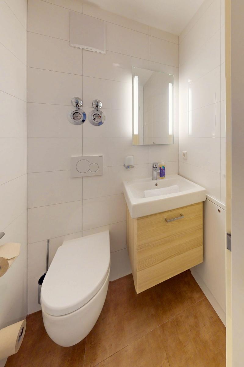Badezimmer mit Toilette, Waschbecken und Spiegel. Holzoptik unter Waschbecken.