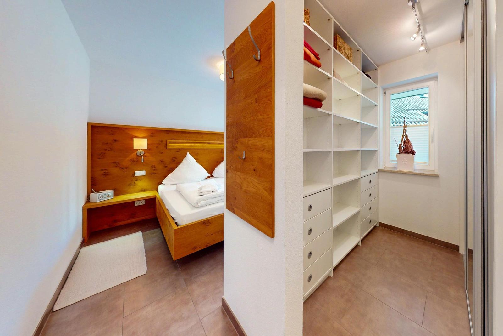 Schlafzimmer mit Holzbett und Kleiderschrank. Fenster mit Pflanze und Licht.