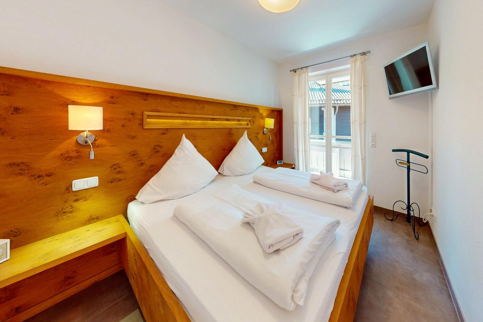 Schlafzimmer mit Bett, Holzwand, TV und Fenster zur Terrasse.