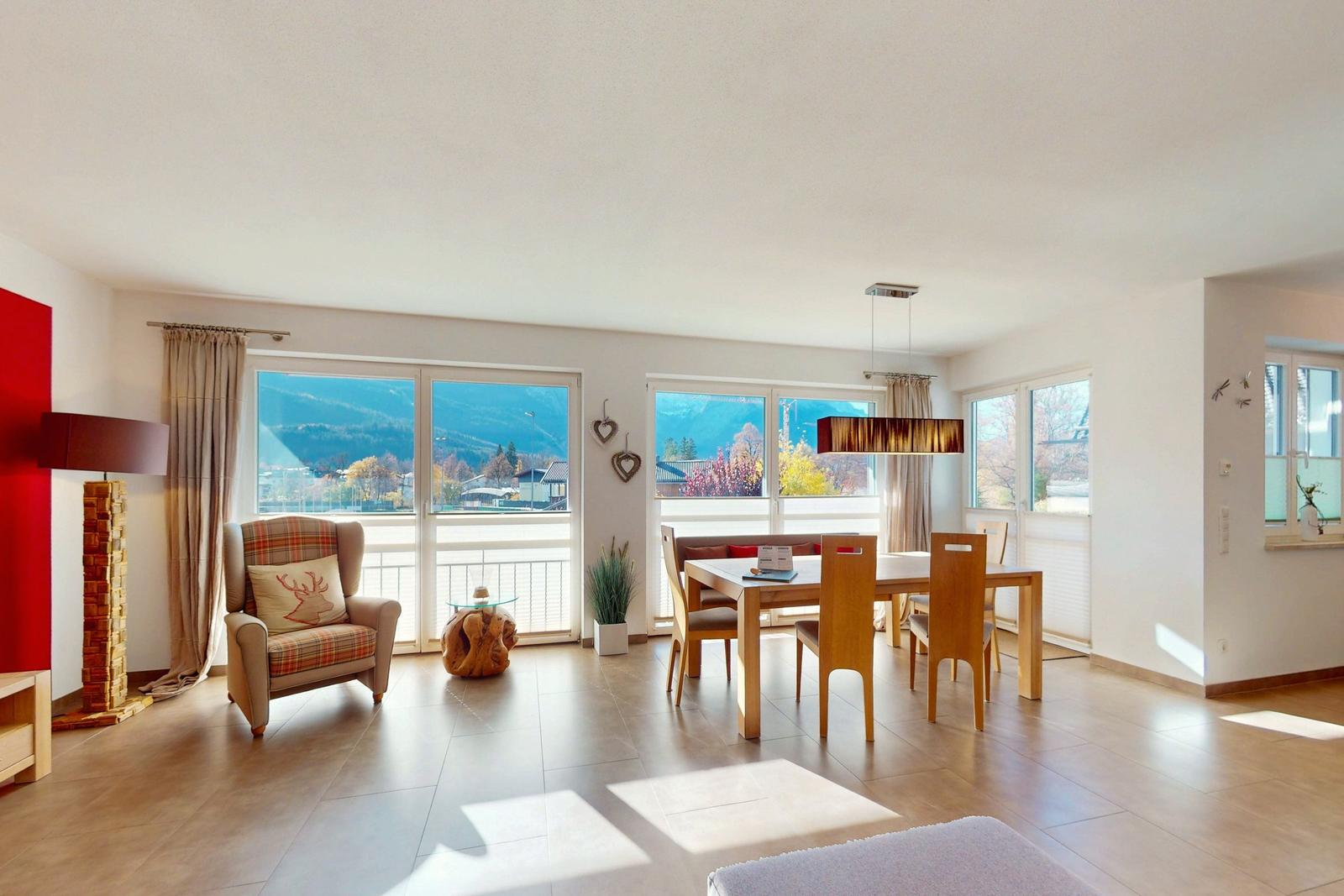 Wohn- und Essbereich mit Blick auf Berge und Balkon. Holzmöbel, Sitzgelegenheiten und Fenster.