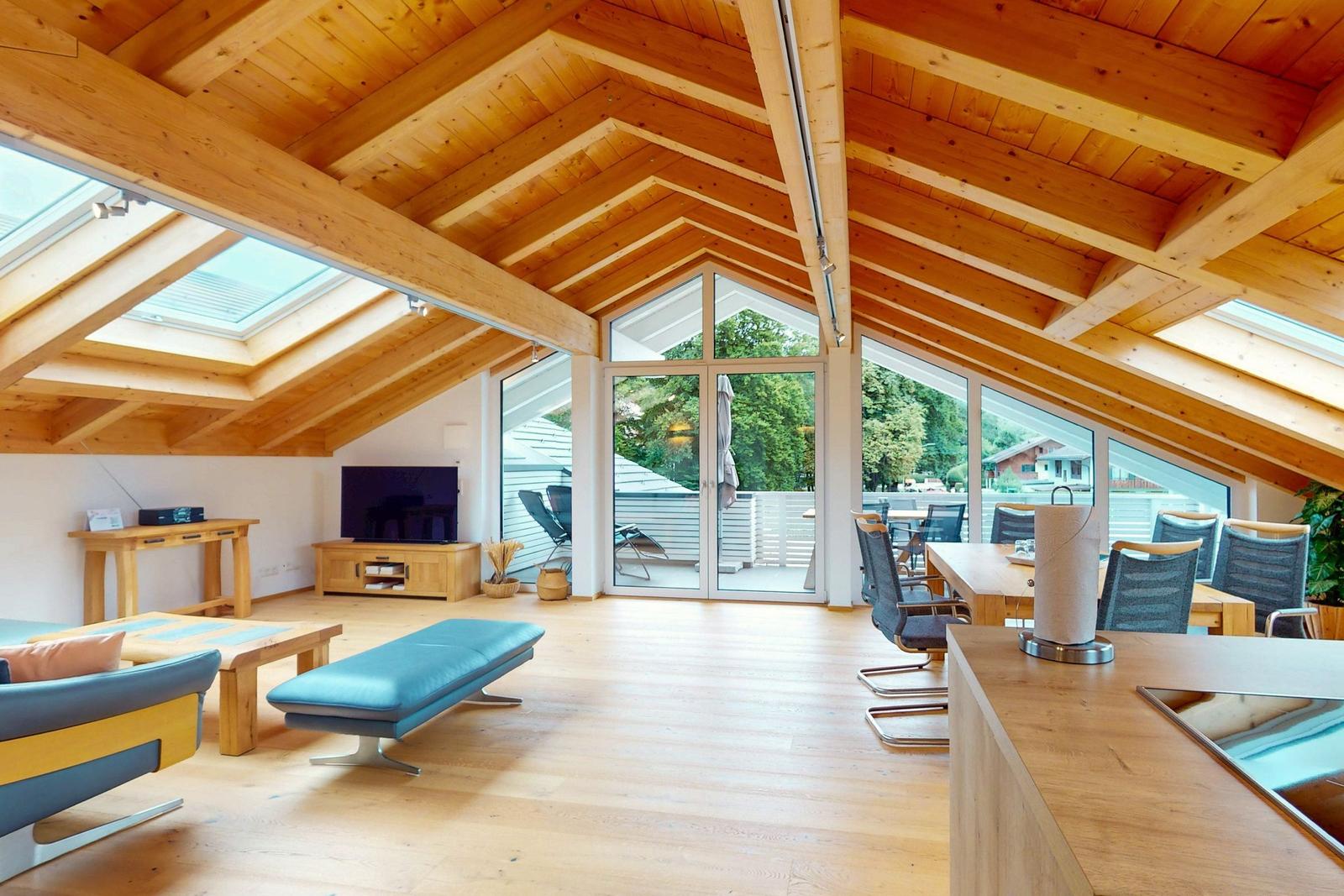Großer Wohn- und Essbereich mit Holzdecke, großen Fenstern und Terrasse.