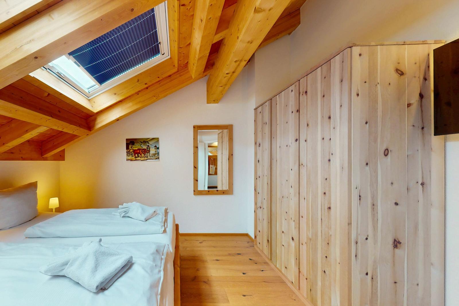 Schlafzimmer mit Dachschrägen, Holzboden und Dachfenster. Holzwand und Spiegel an der Wand.