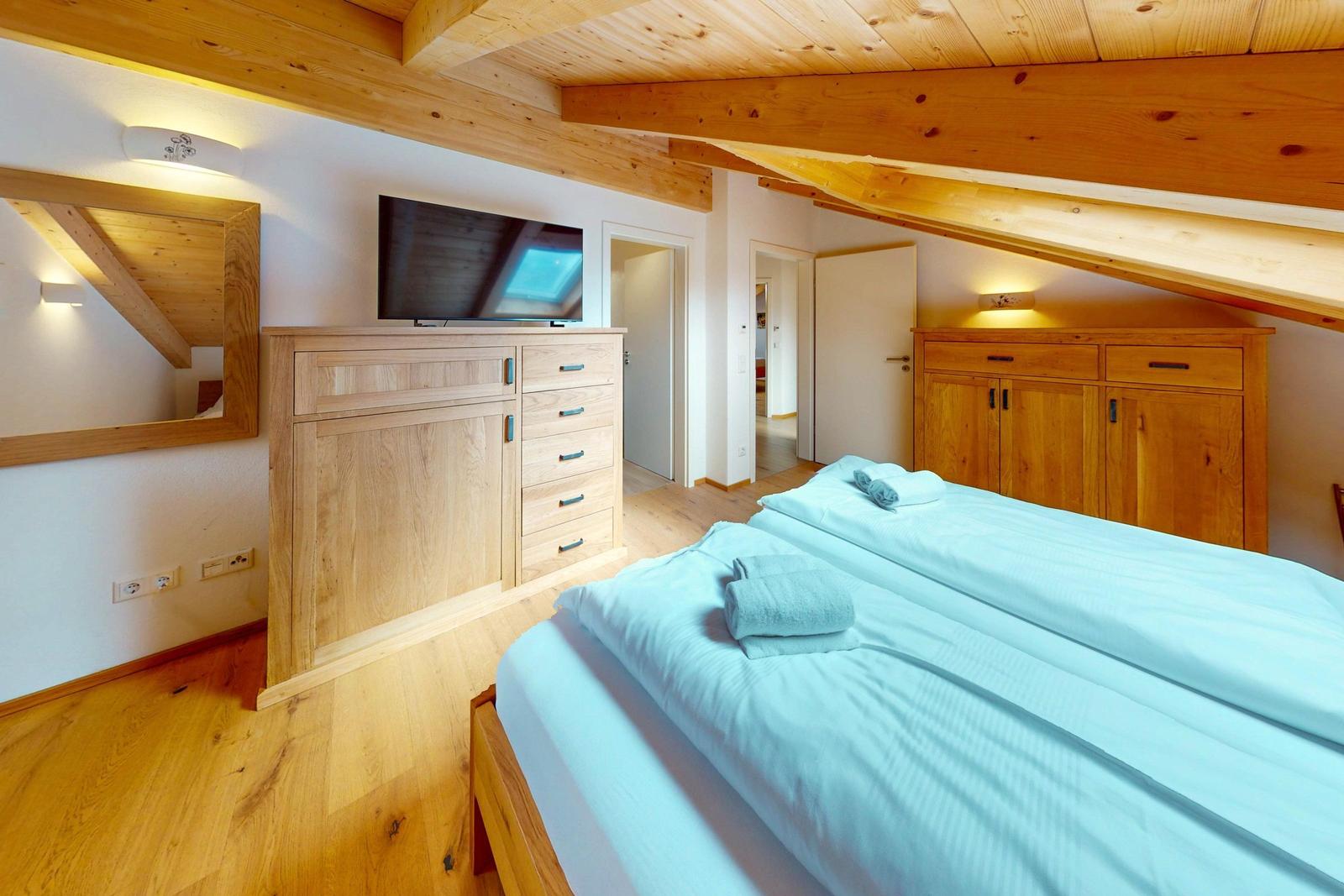 Schlafzimmer mit Holzboden, Bett, Kleiderschrank und Fernseher unter Holzdecke.
