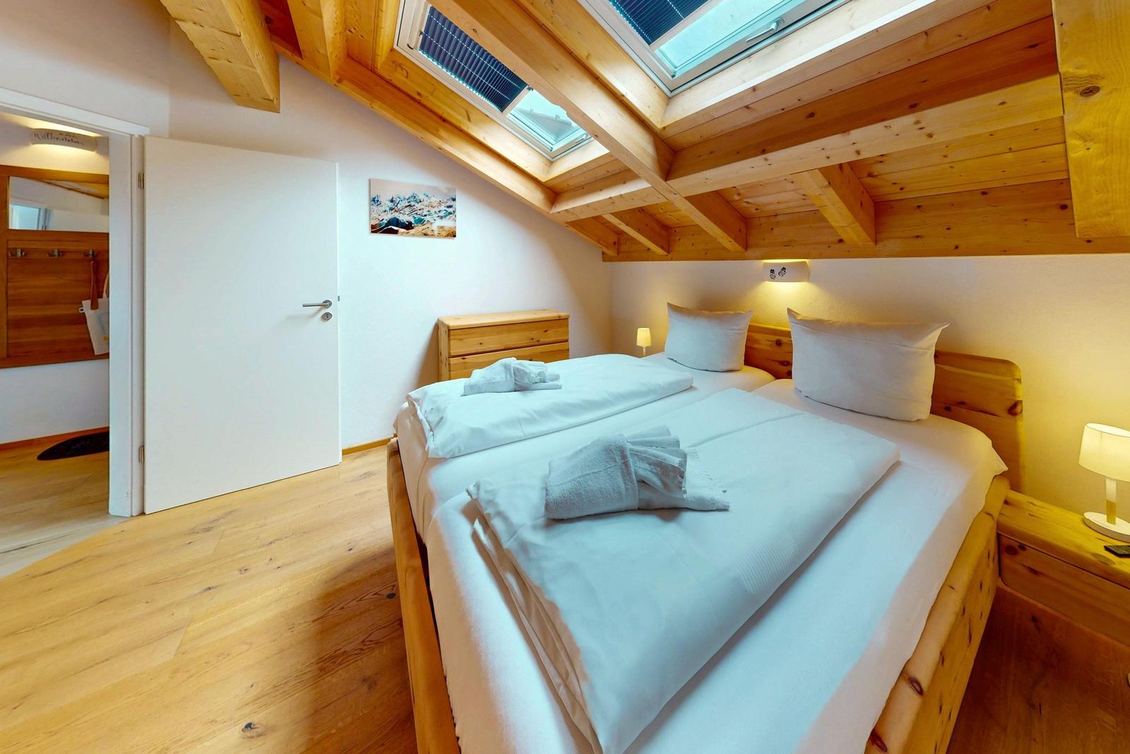 Schlafzimmer mit Doppelbett, Holzboden und Dachschrägen mit Fenstern.