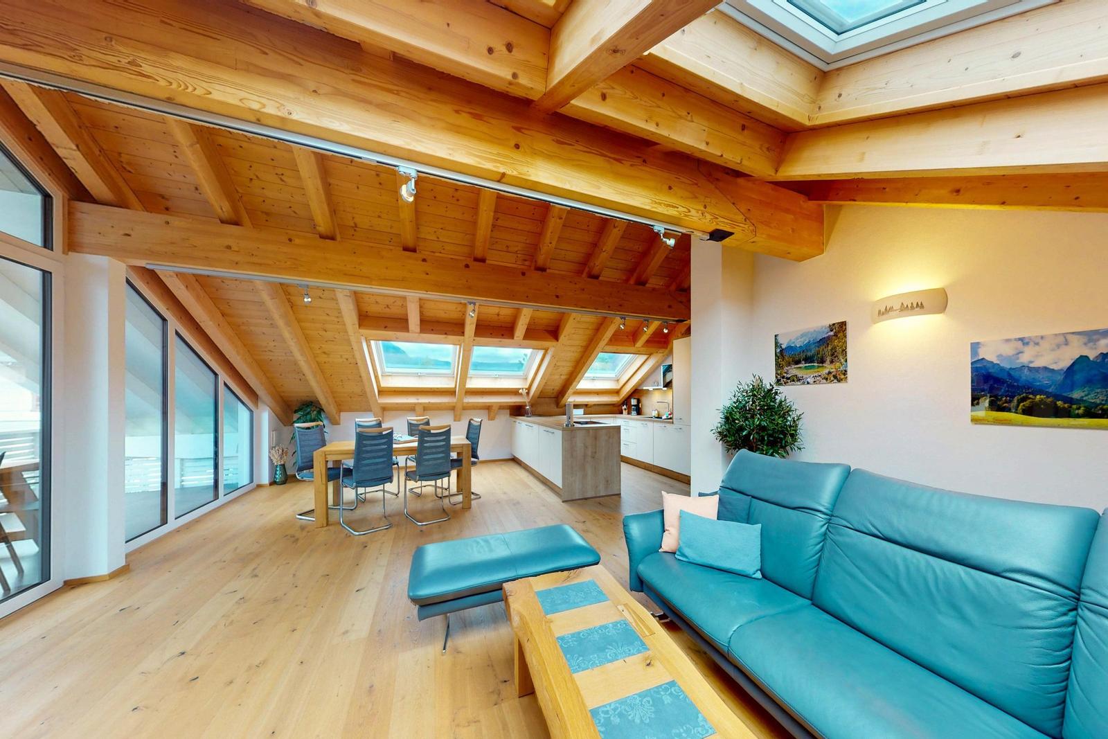 Wohn- und Essbereich mit Holzboden, blauem Sofa und Dachfenstern.