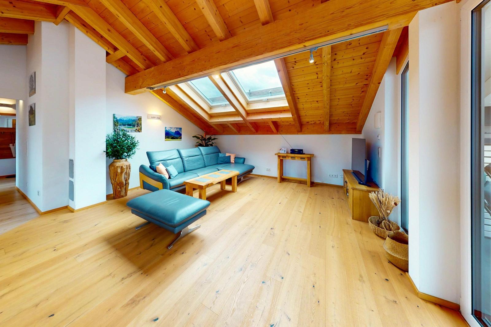 Wohnraum mit Holzboden, blauem Sofa und Dachfenstern unter Holzdecke.