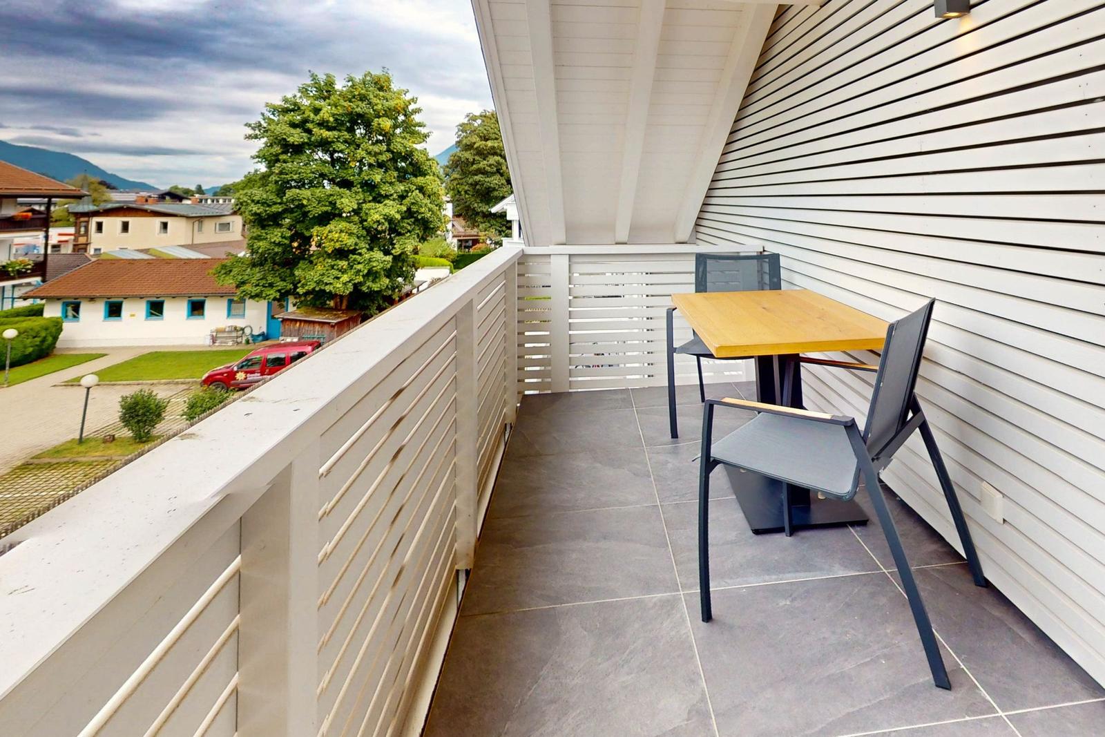 Terrasse mit Tisch und zwei Stühlen, Blick auf Grünfläche und Gebäude.