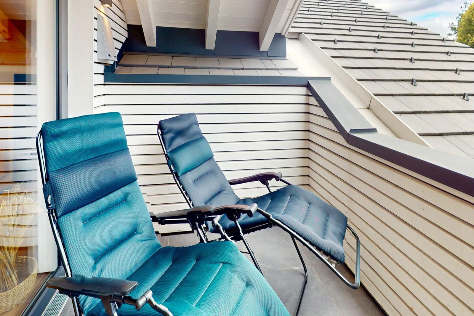 Zwei blaue Liegestühle auf einer Terrasse neben einem Haus mit weißen Schindeln.