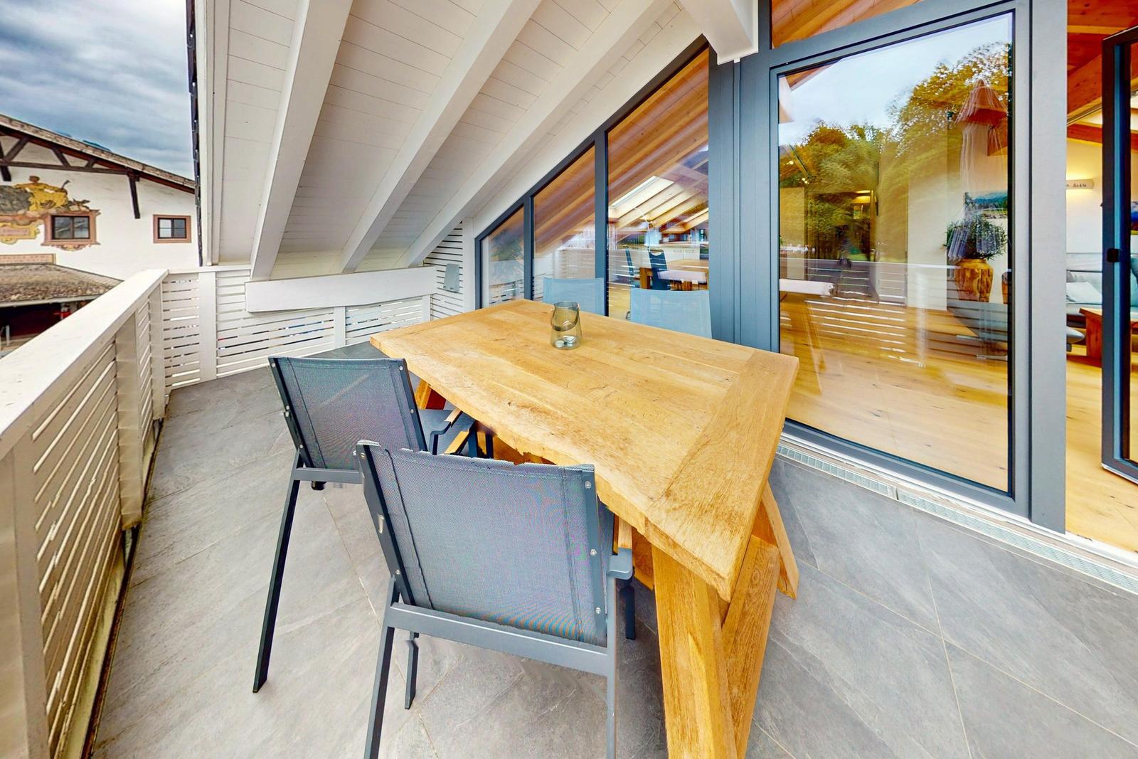 Terrasse mit Holztisch und Stühlen, Blick in Wohnbereich mit Holzboden und Glasfront.