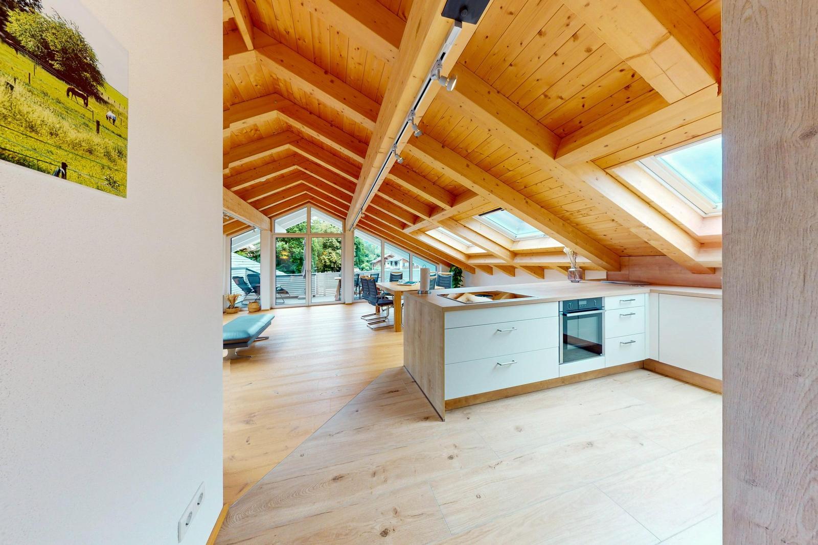 Küche mit Holzboden und Dachschrägen. Durchgang zum Essbereich mit Tisch und Stühlen.