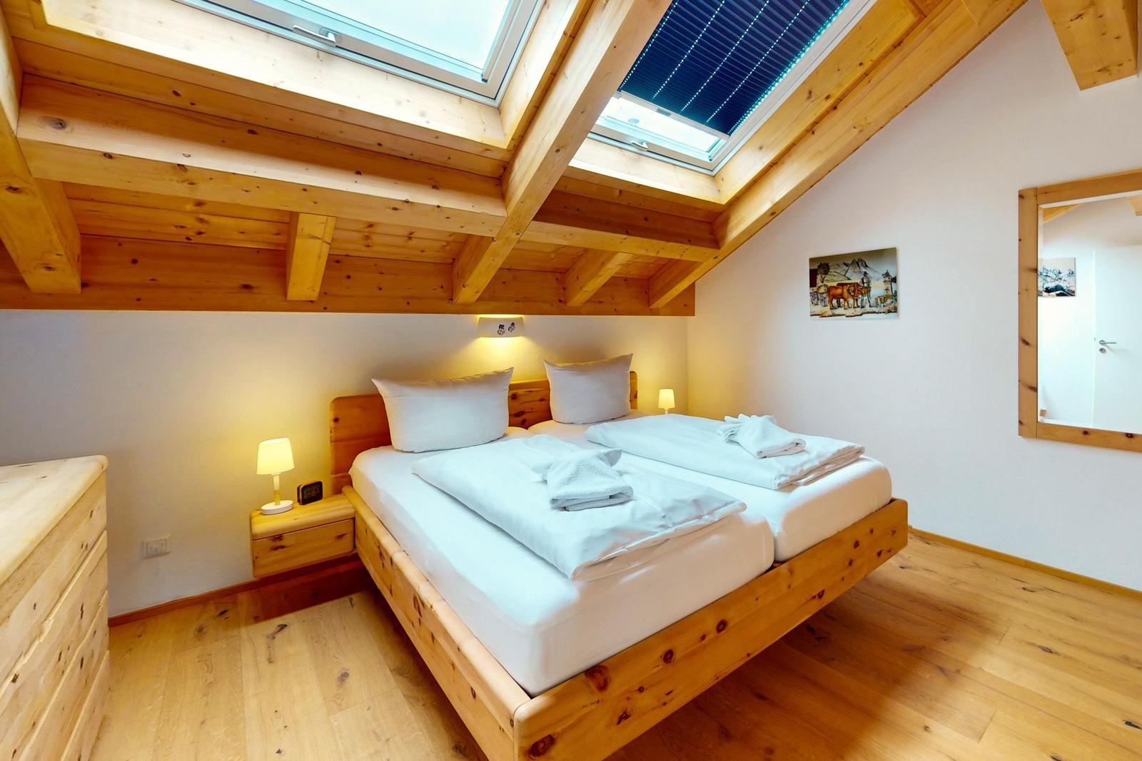 Schlafzimmer mit Doppelbett, Holzboden und Dachfenstern. Wandbild und Spiegel sind vorhanden.