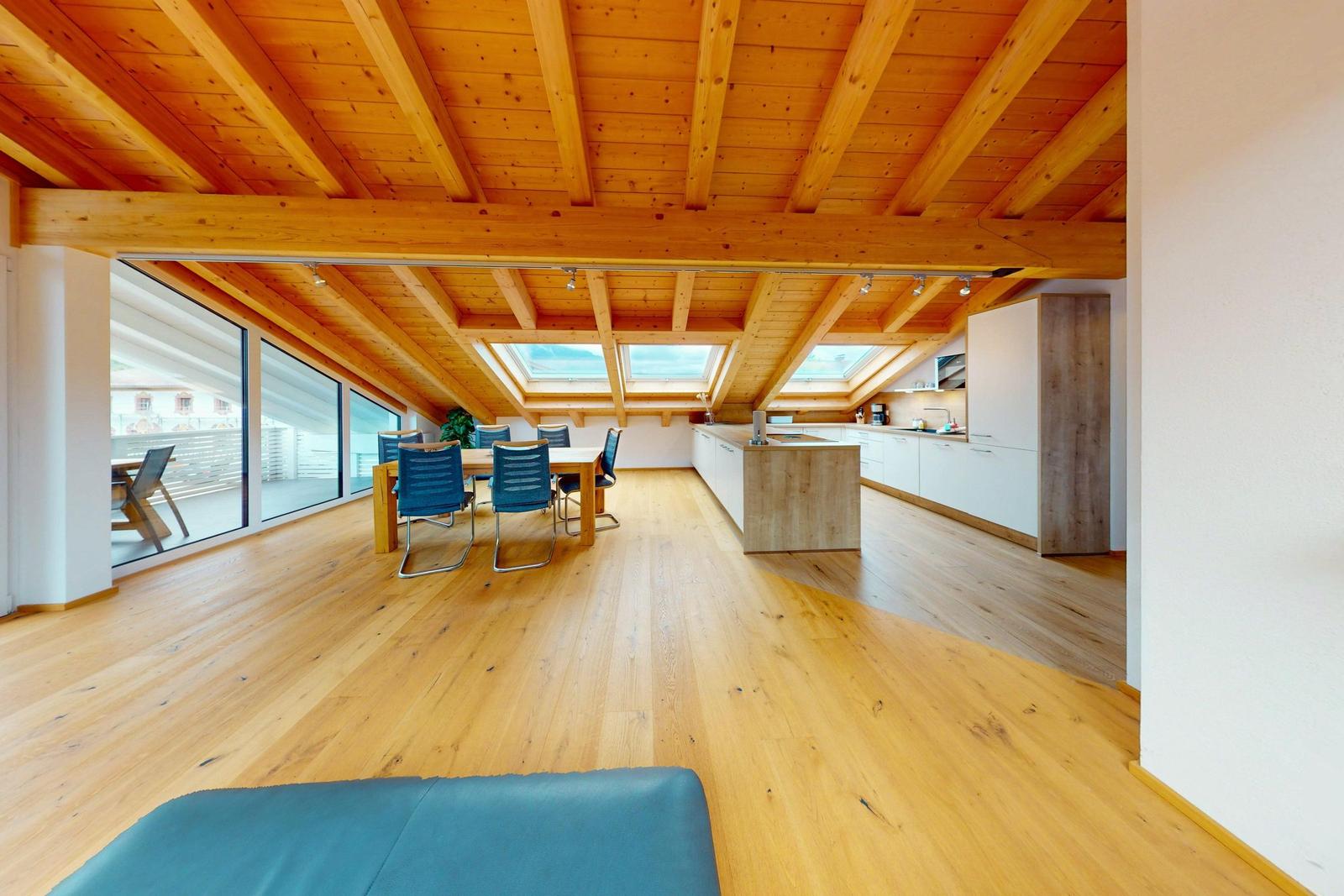 Offener Raum mit Holzboden, Essbereich und Küche unter Holzdecke mit Dachfenstern.