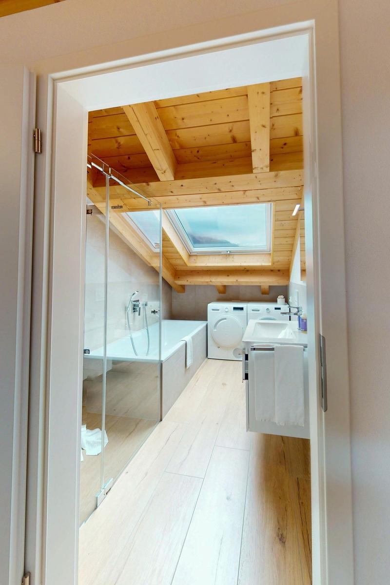 Dusche, Badewanne und Waschmaschine in Dachschrägen-Bad mit Holzdecke und Dachfenster.