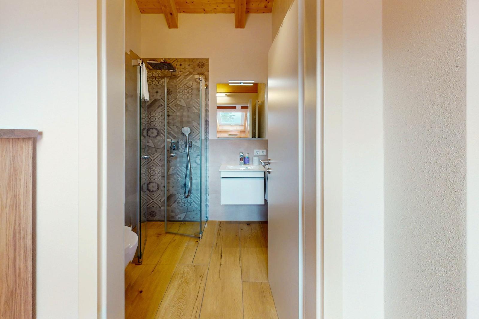 Badezimmer mit Dusche, Waschbecken und Toilette. Holzfußboden und Holzbalken an der Decke.