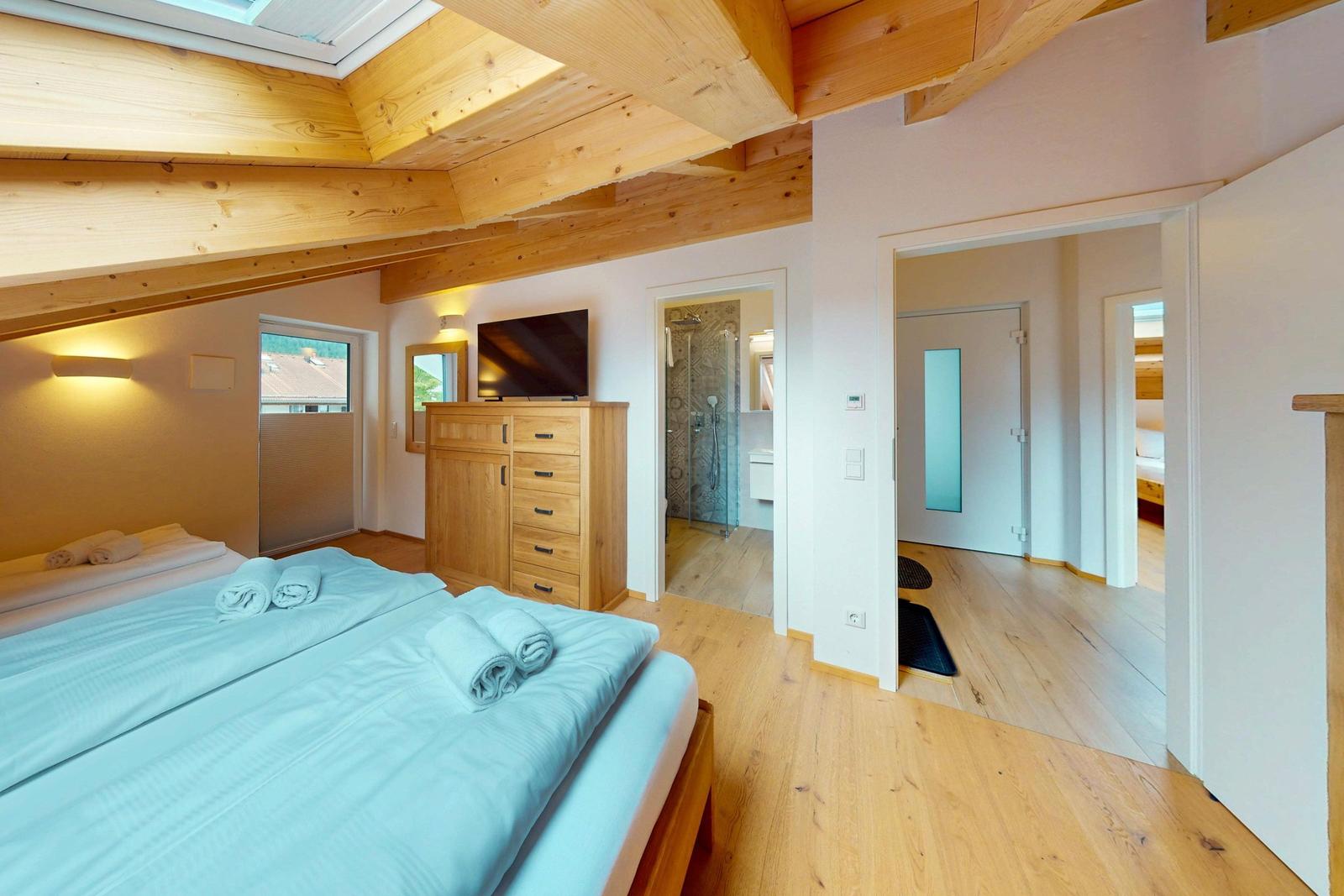 Schlafzimmer mit Holzboden, Dachschrägen und TV. Blick in Bad und angrenzenden Raum.