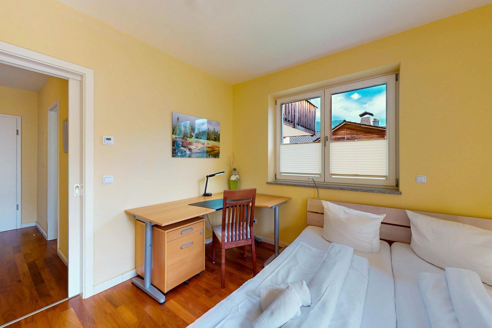 Ein Schlafzimmer mit Doppelbett, Schreibtisch und Fenster mit Blick auf Holzhaus.