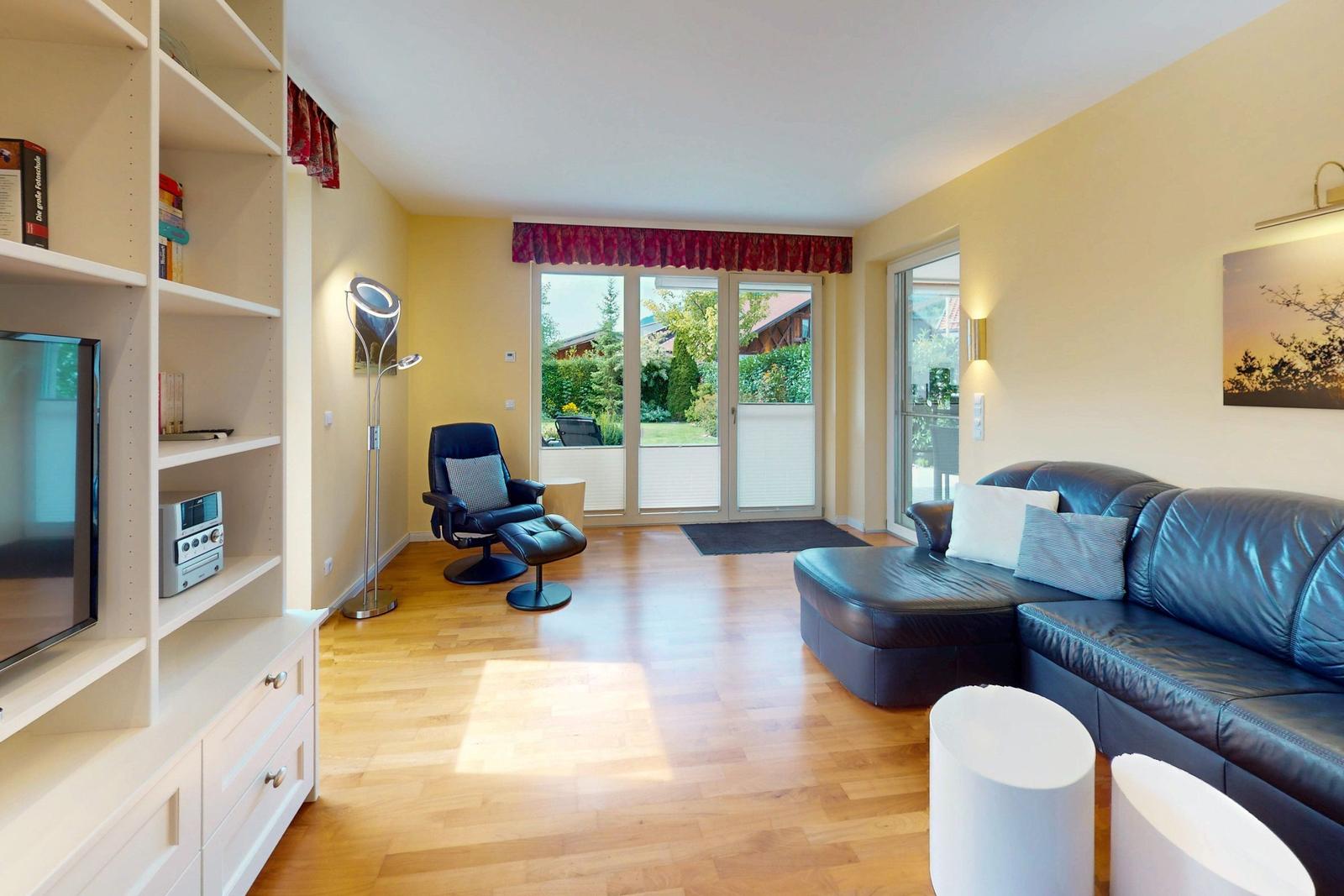 Wohnzimmer mit Ledersofa, Sessel, Bücherregal und Blick auf den Garten.