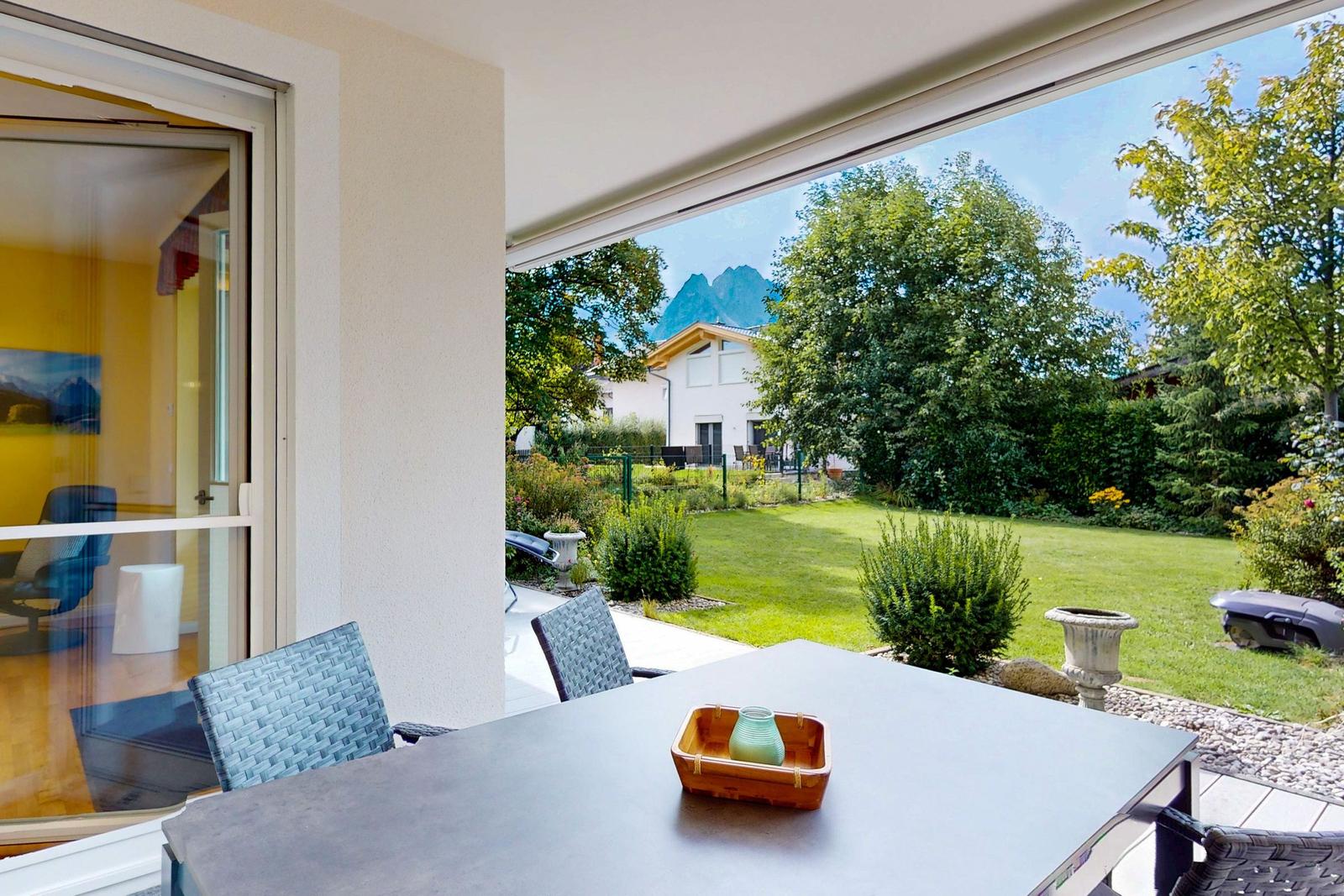 Terrasse mit Tisch und Stühlen, Blick auf Garten und Berge.