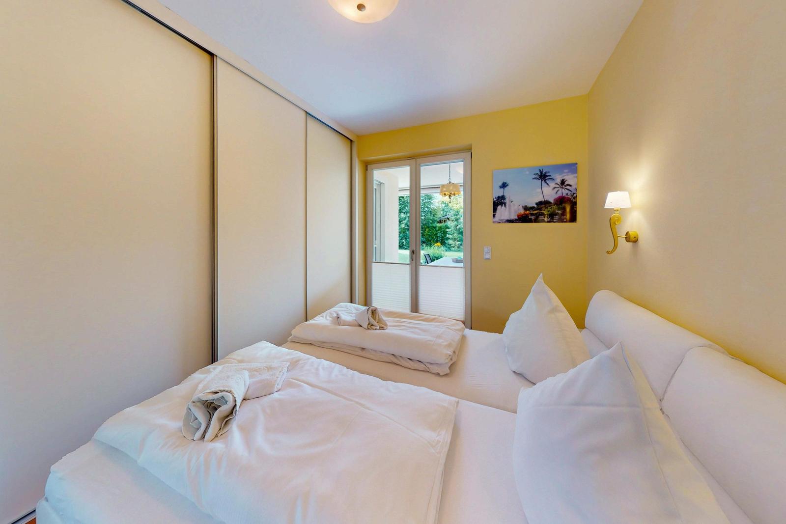 Schlafzimmer mit Bett, Schrank und Balkontür. Wandbild und Wandlampe sichtbar.