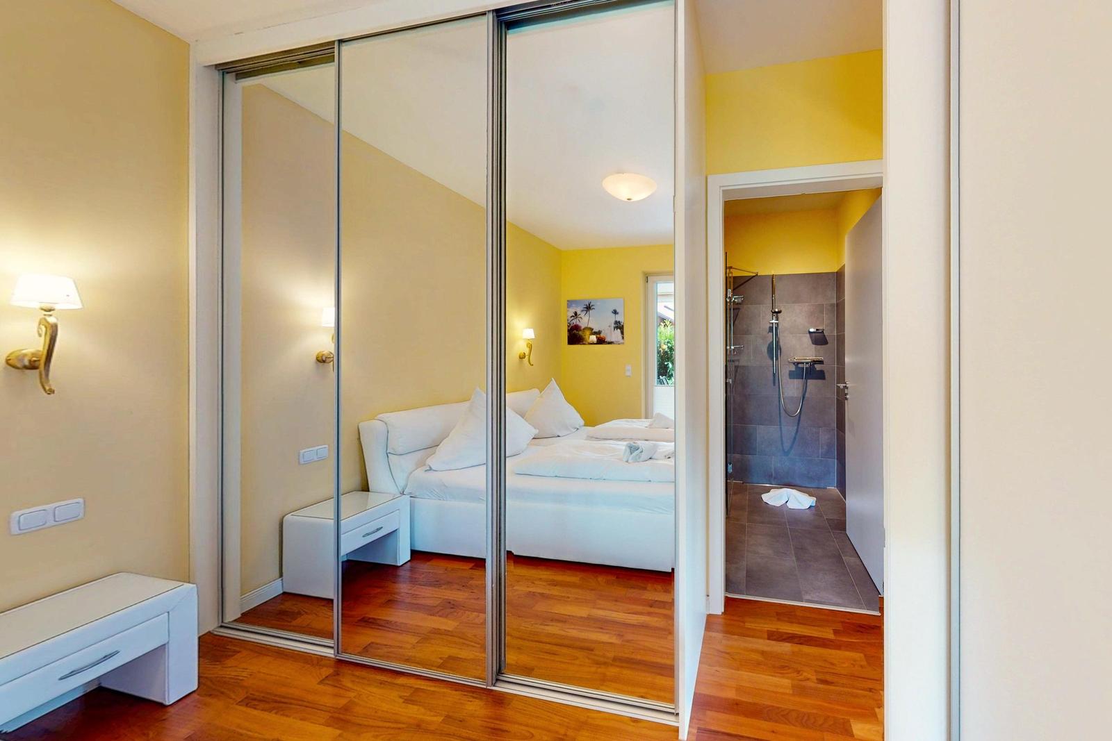 Schlafzimmer mit Dusche und Spiegeltüren. Holzboden und gelbe Wände.