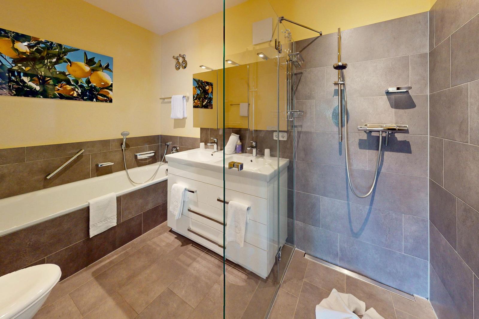Badezimmer mit Badewanne, Dusche und Waschtisch. Wandbild mit Zitronen.