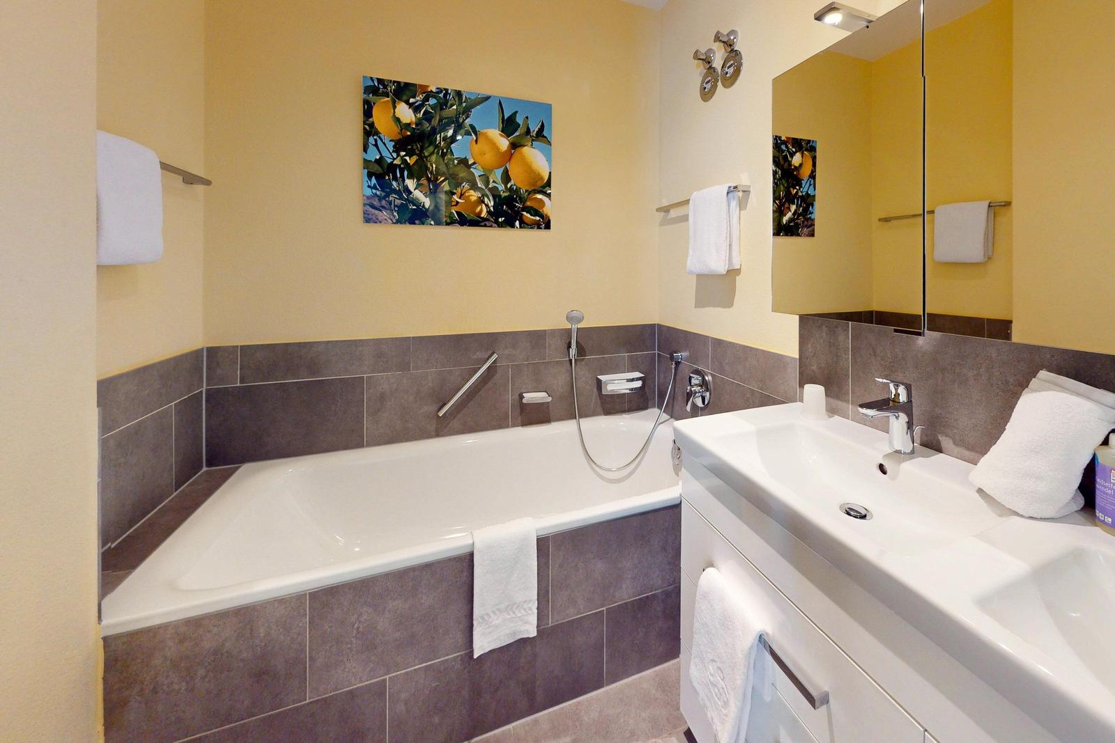 Badezimmer mit Badewanne, Waschbecken und Spiegel. Wandbild mit Zitronen.