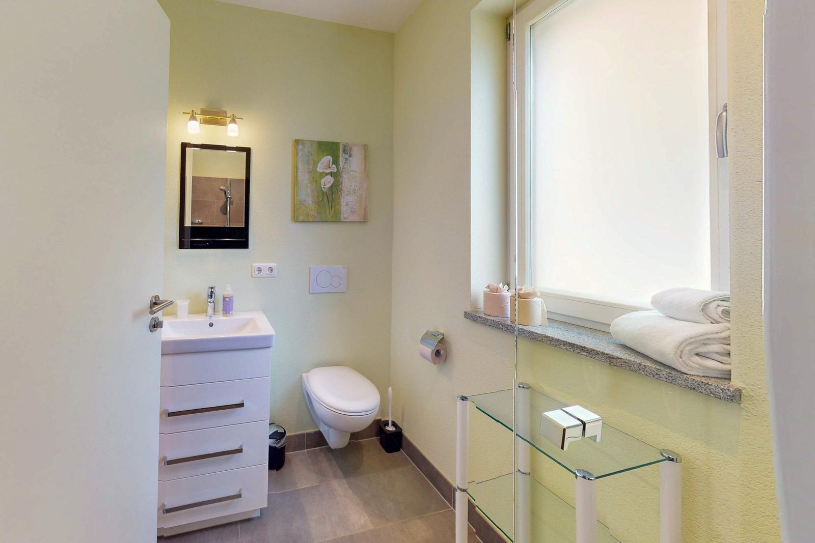 Badezimmer mit Dusche, Waschbecken und Toilette. Fenster mit Handtüchern.