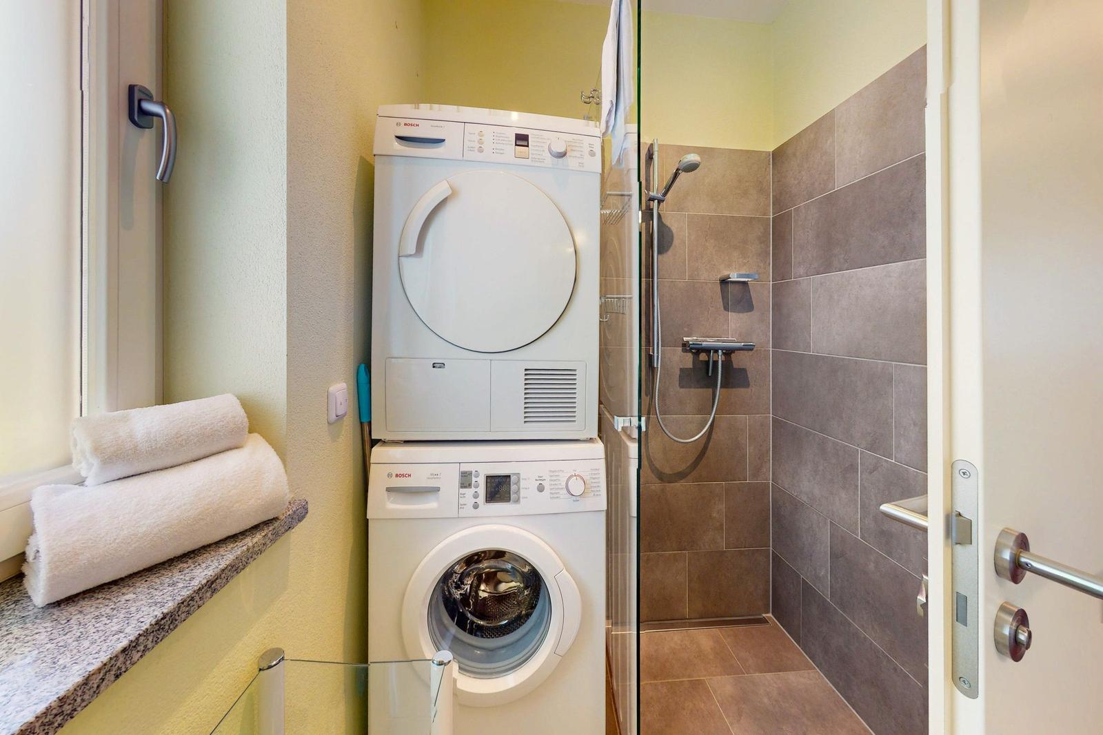 Waschmaschine und Trockner in einem Badezimmer mit Dusche und Handtüchern.