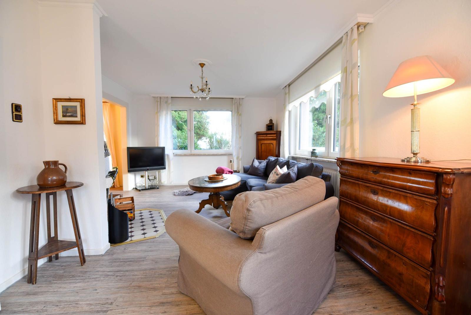 Wohnzimmer mit Sofa, Couch, TV und Holzmöbeln. Fenster mit Blick auf Garten.