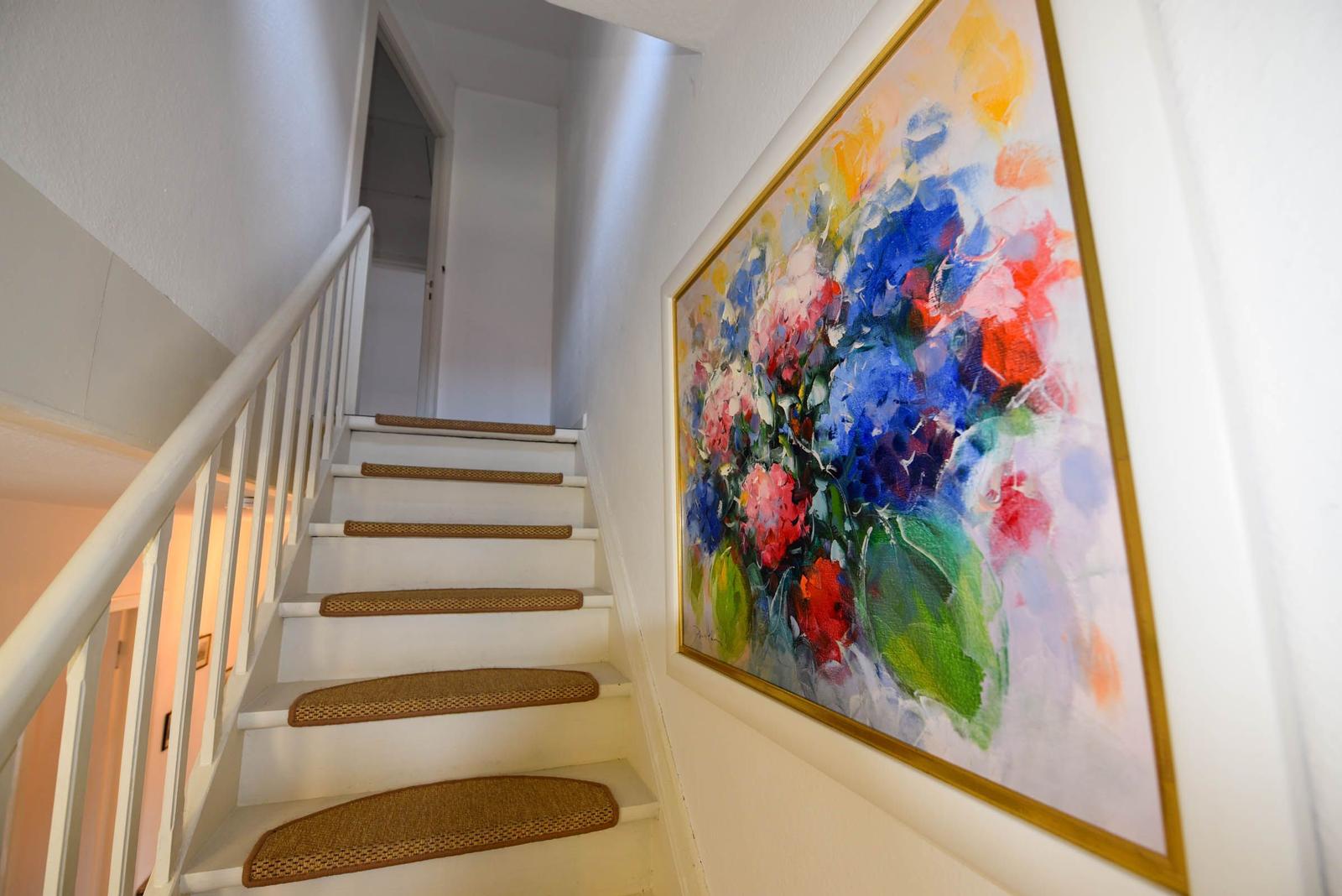 Treppenhaus mit weißer Treppe und buntem Wandbild.