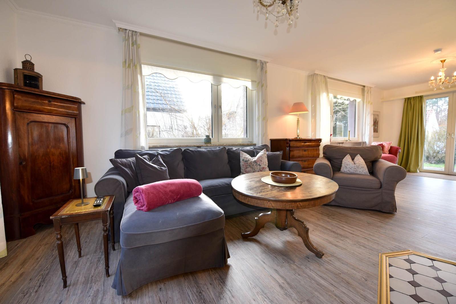 Wohnzimmer mit Sofa, Sessel und Holztisch. Fenster und Tür zur Außenterrasse.