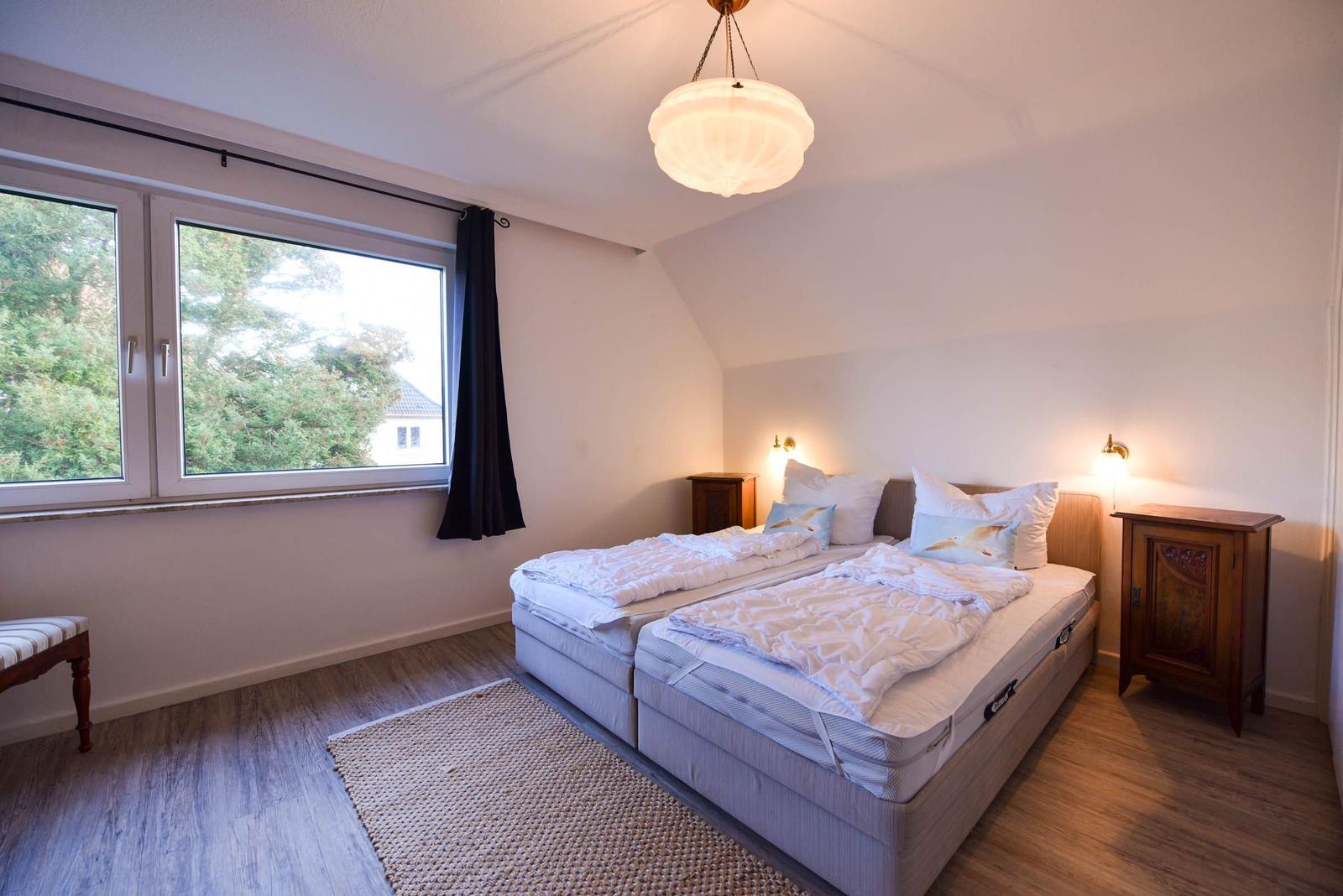 Schlafzimmer mit Doppelbett, Holzboden und großem Fenster mit Blick auf Bäume.