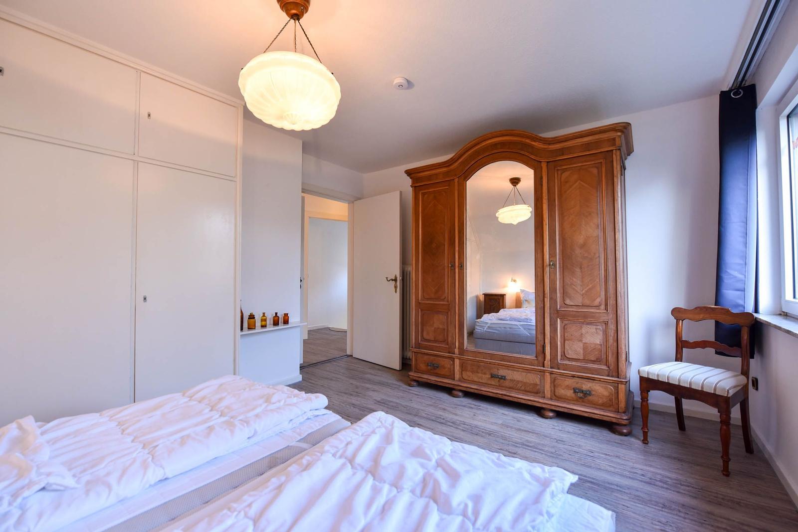 Zwei Betten, ein Holzschrank mit Spiegel und eine Stuhl am Fenster.