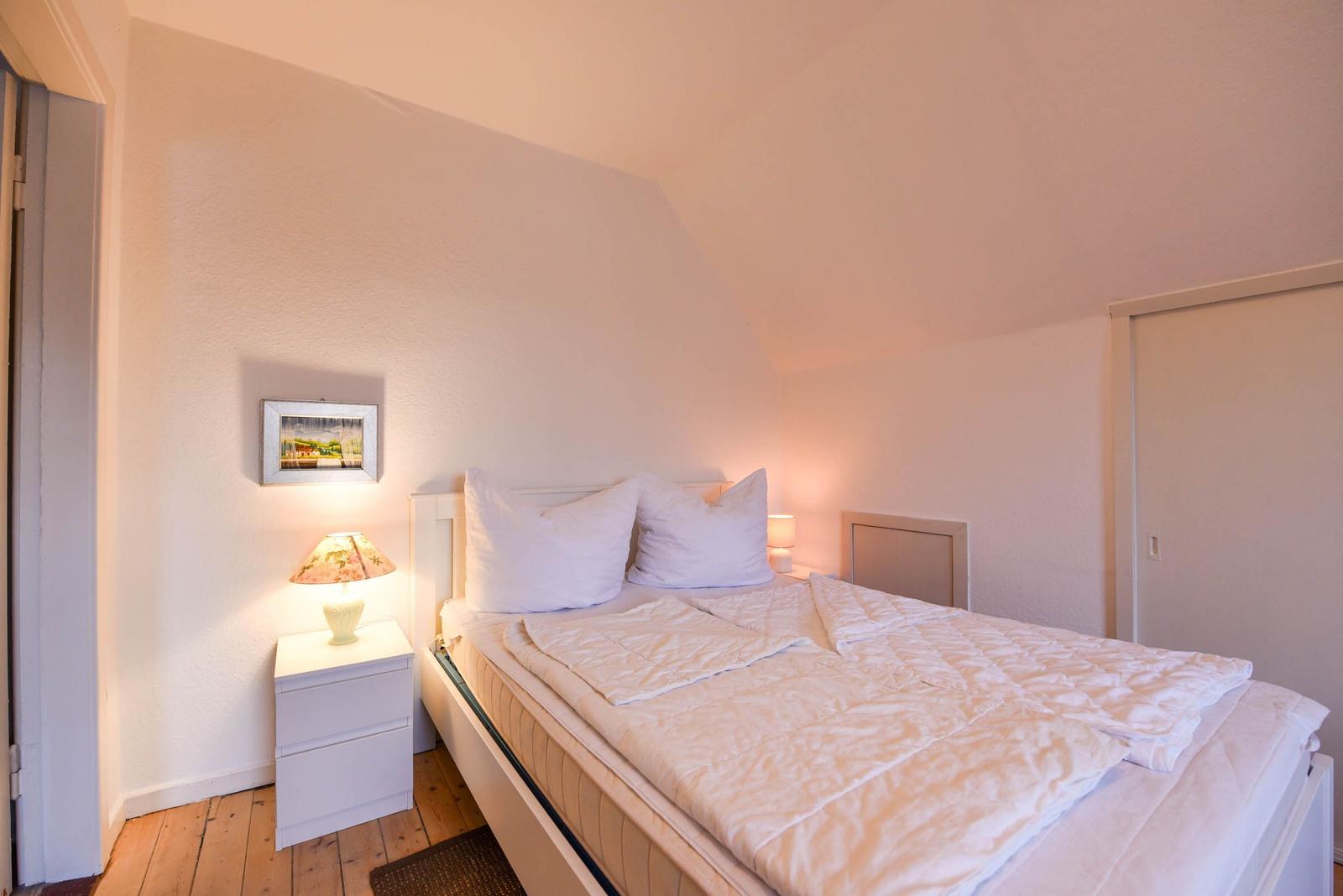 Schlafzimmer mit Bett, Nachttisch und Lampen. Holzboden und Schrankschrank.
