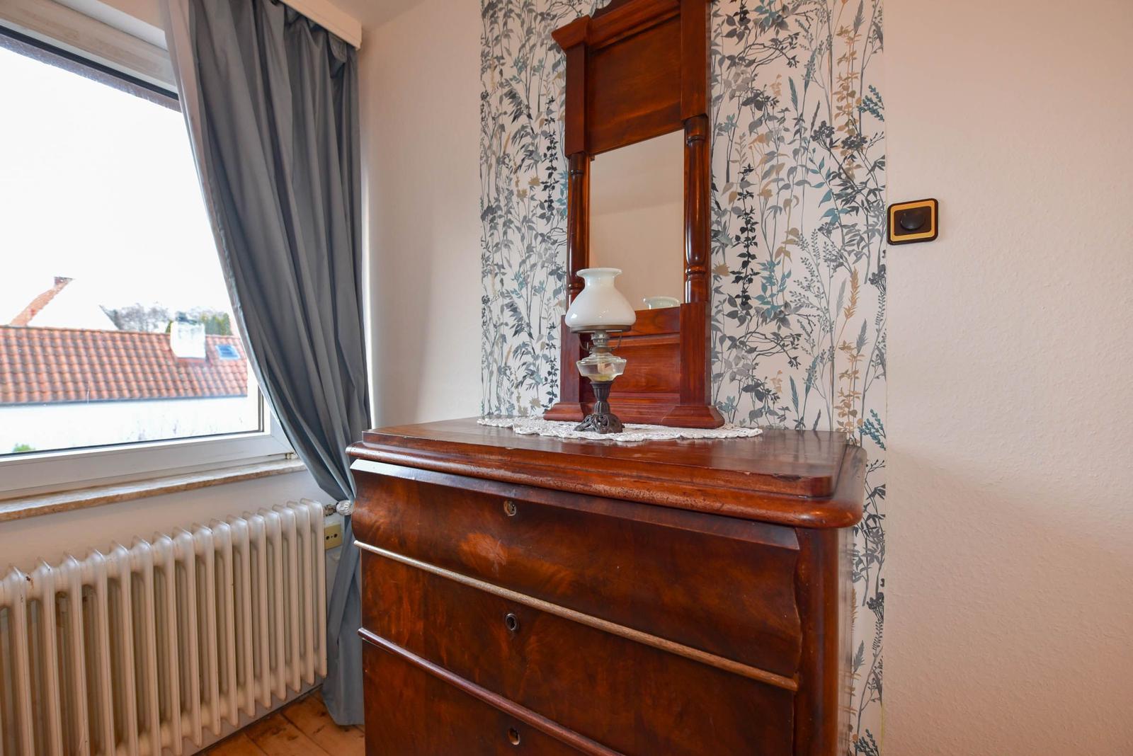 Holzschrank mit Spiegel und Lampe vor floraler Tapete
