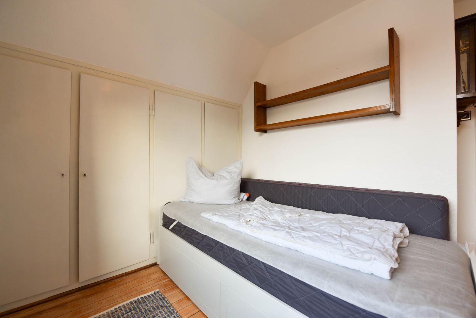 Schlafzimmer mit Bett, Kleiderschrank und Wandregal.