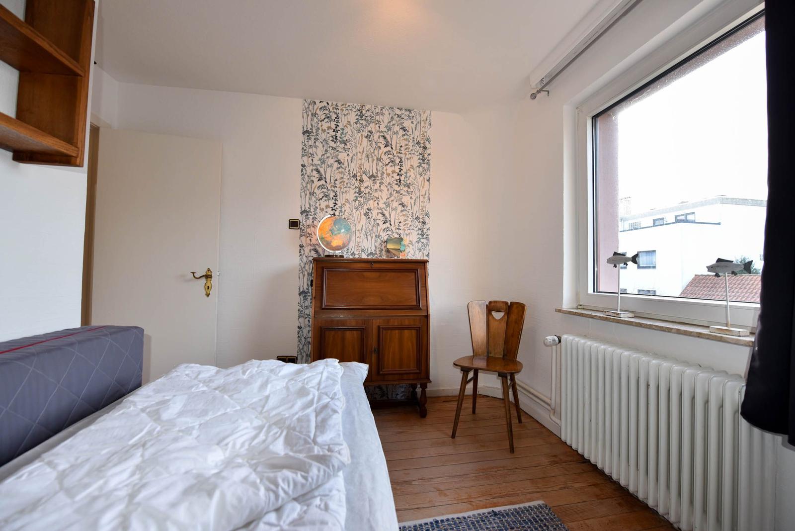 Schlafzimmer mit Bett, Holzfußboden, Schrank und Fenster mit Blick auf Gebäude.