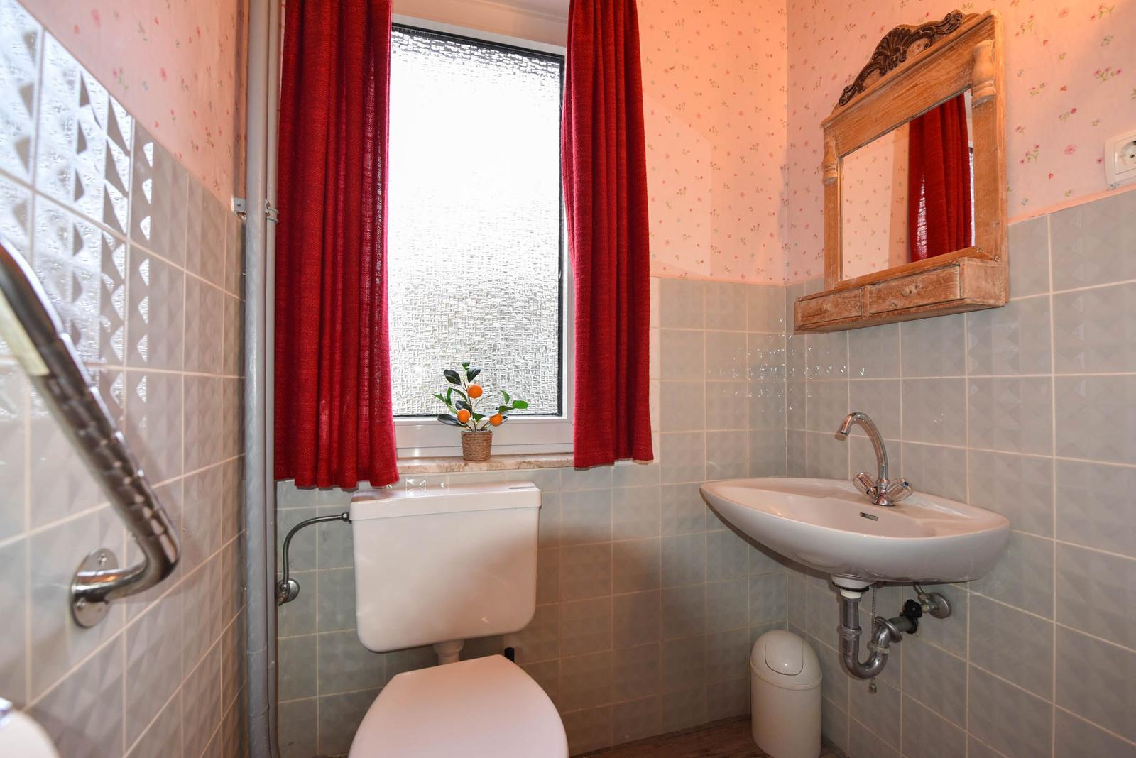 Badezimmer mit Toilette, Waschbecken und Fenster mit roten Vorhängen.